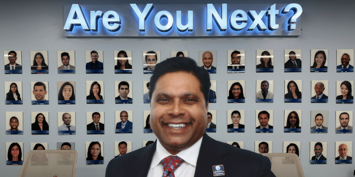 Dr. Michael Everest in a suit and tie standing in front of his “Are You Next?” wall in his conference room.